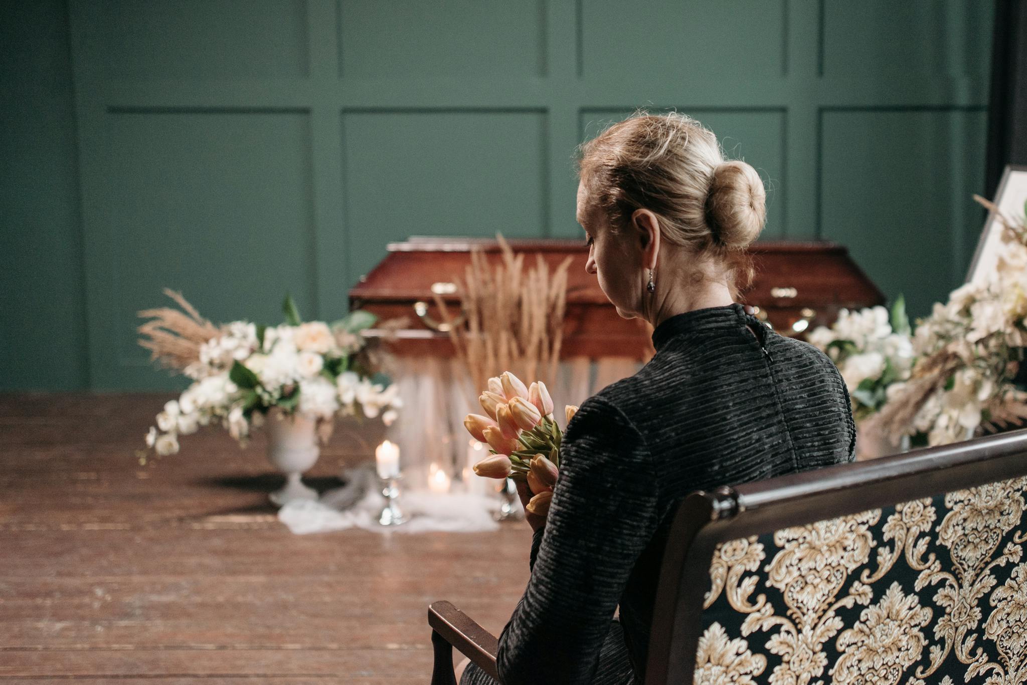 A woman in mourning holding flowers at a funeral, highlighting grief and remembrance.